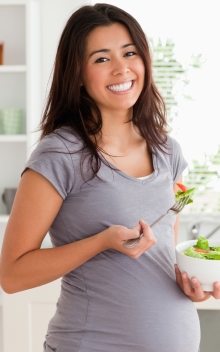 Attractive pregnant woman holding a bowl of salad while standing