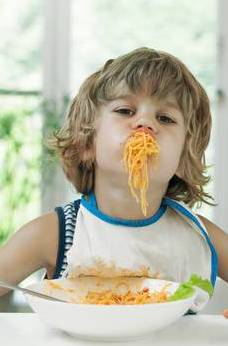 Portrait of a cute young boy making a mess while eating pasta for lunch