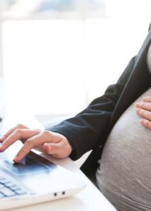 Pregnant woman working on laptop. Cropped image of pregnant businesswoman typing something on laptop while sitting at her working place in office