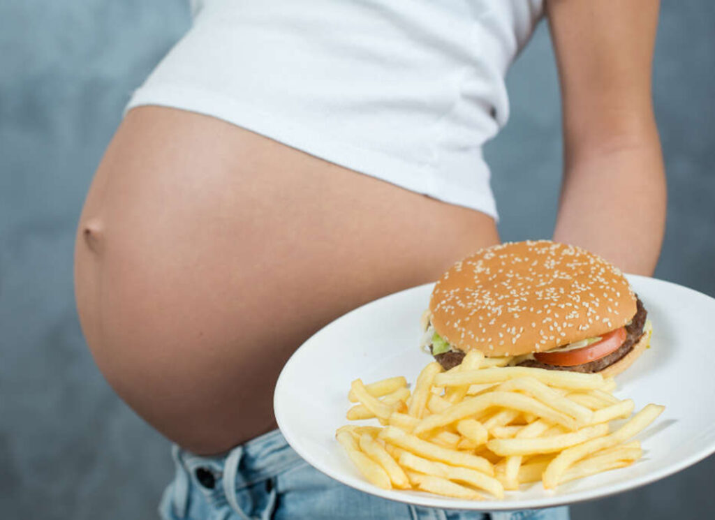 Close up of a cute pregnant belly and junk food. Hamburger and p